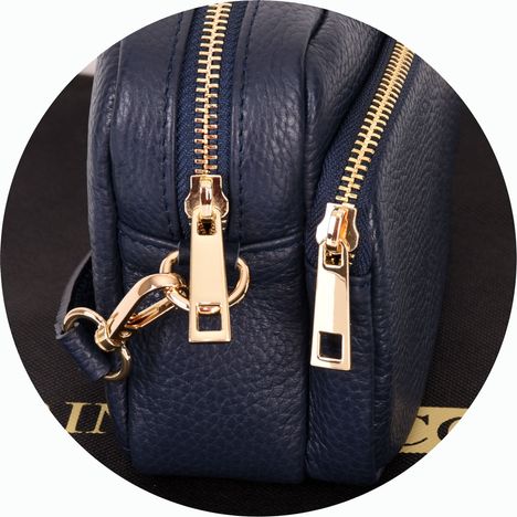 close up of chunky gold metal zip pullers on a womens navy blue leather small shoulder bag